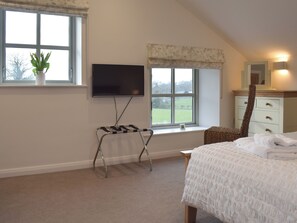 A bedroom with a bed, a TV mounted on the wall, a window with a view of a green field, and a dresser with drawers.