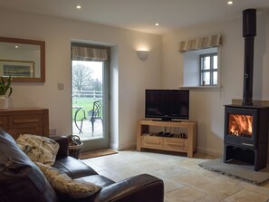 A living room with a sofa, a TV on a wooden stand, a fireplace, and a view of the outdoors. - Five Barred Gate Barn (Whitechapel, near Goosnargh)