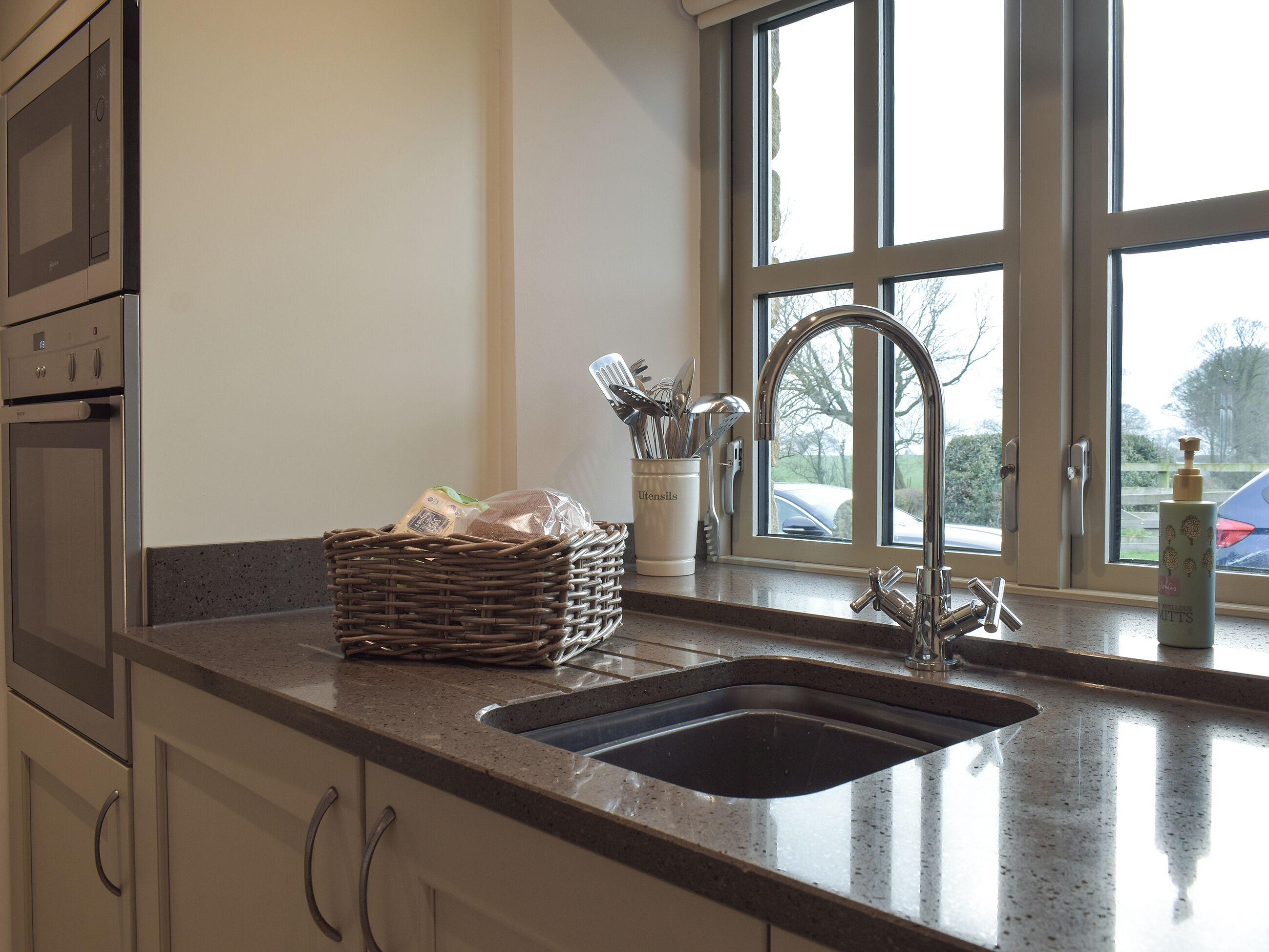 A kitchen with a stainless steel sink, a wicker basket, and utensils on the counter.