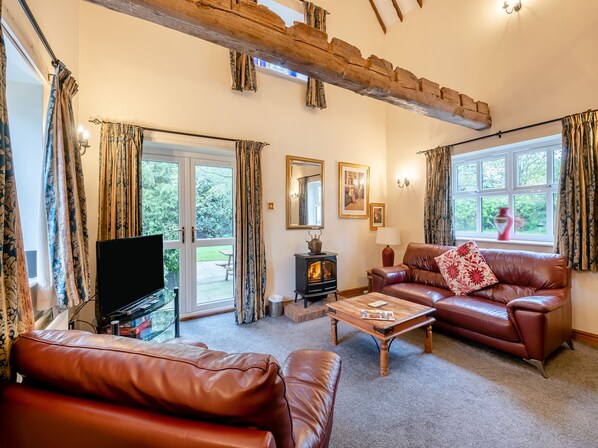 A cozy living room with leather sofas, a wooden coffee table, a television, a fireplace, and large windows with curtains. - 3 bedroom accommodation in York (York)
