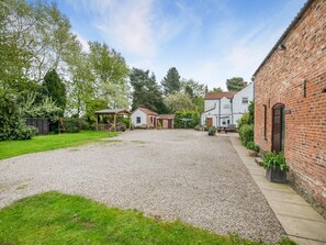 A gravel driveway leading to a white house with a brick extension, surrounded by greenery and a covered seating area. - 3 bedroom accommodation in York (York)