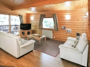 A log cabin interior with two white sofas, a coffee table, a TV on a wooden cabinet, and a view of the outdoors through large windows. - Perfectly set in Kenwick Woods, an idyllic peaceful retreat. (Kenwick, near Louth)