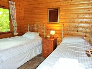 Et hyggeligt træhusværelse med to senge, et natbord med lampe og et vindue med gardiner.