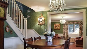 A dining area with a round wooden table and six chairs, a chandelier, and a staircase with white railings.
