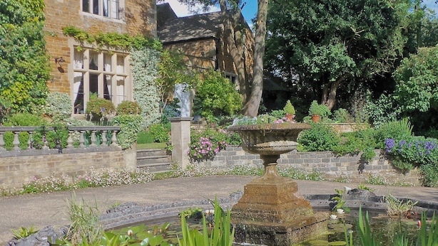 A stone fountain surrounded by a garden with a variety of plants and flowers.