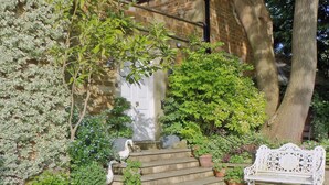 A stone staircase leading to a white door, surrounded by potted plants and a white bench.