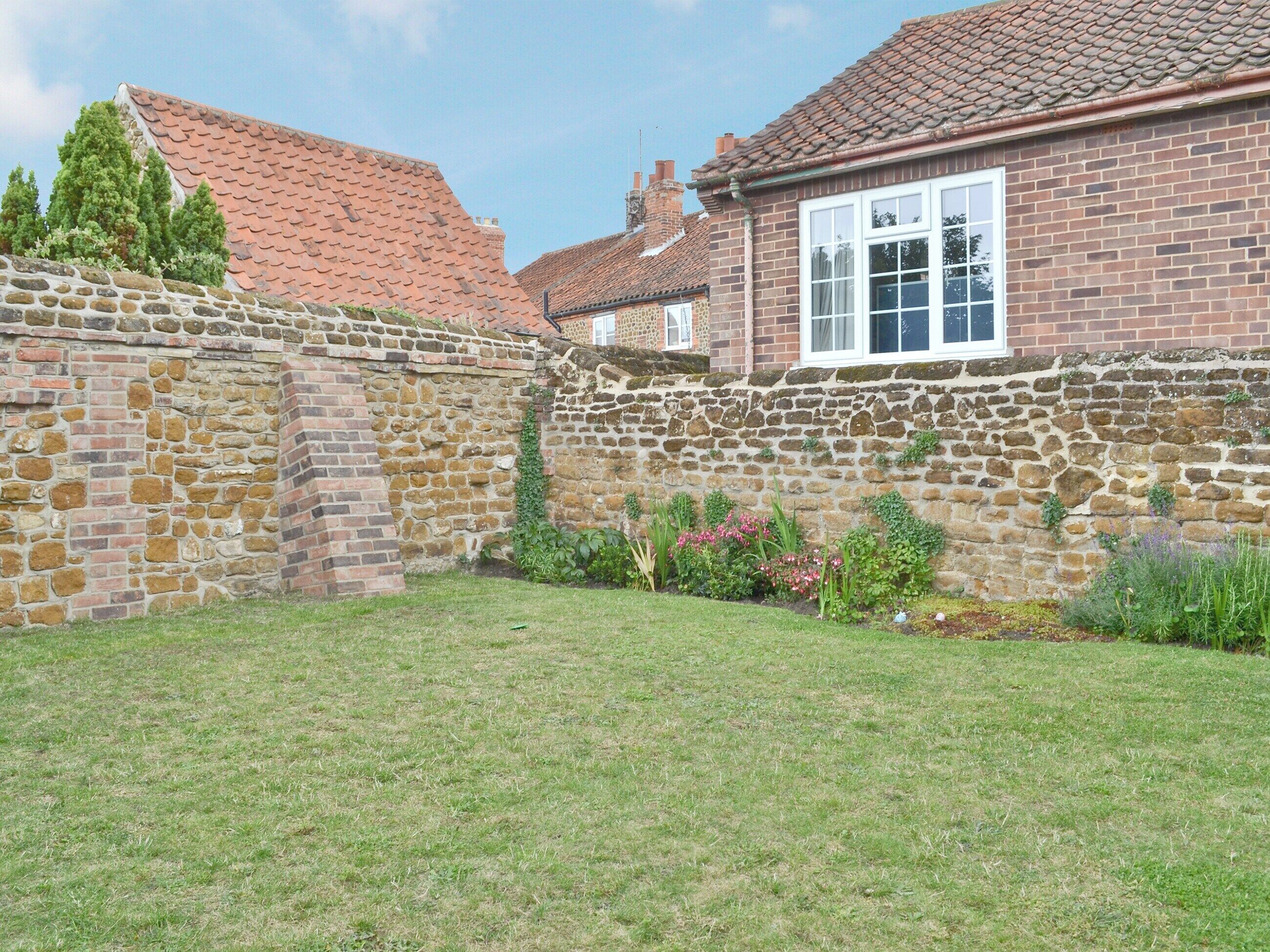 A stone wall with a brick house, a grassy yard, and a clear sky.