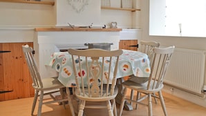 A dining area with a table set for four, surrounded by wooden chairs. Above the table, there are decorative items on shelves, including a heart-shaped ornament with the word "LOVE" and two bird-shaped decorations. - 2 bedroom accommodation in Heacham, near King&rsquo;s Lynn (Heacham, near King&rsquo;s Lynn)