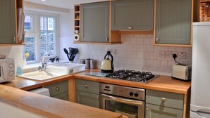 A modern kitchen with a gas stove, oven, and sink. There are wooden cabinets and a window providing natural light. - 2 bedroom accommodation in Heacham, near King&rsquo;s Lynn (Heacham, near King&rsquo;s Lynn)