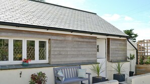 Une maison avec un toit recouvert de tuiles grises, un revêtement en bois, un banc et des plantes en pot.