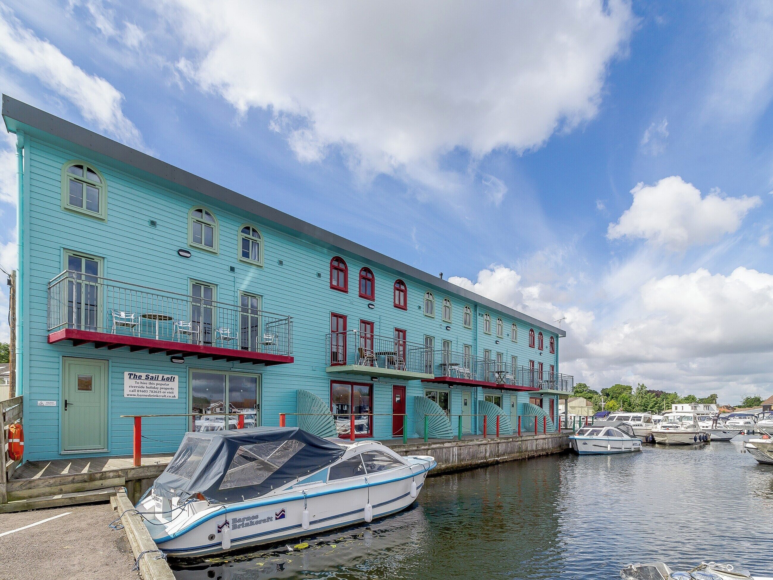 Un bâtiment turquoise doté de nombreux balcons, un quai avec un bateau, et une marina en arrière-plan.