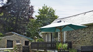 A stone building with a wooden fence, a patio with a table and chairs, and a green umbrella.