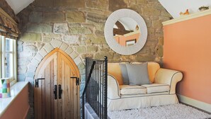 Una habitación acogedora con pared de piedra, puerta de madera, un banco acolchado y un espejo redondo.