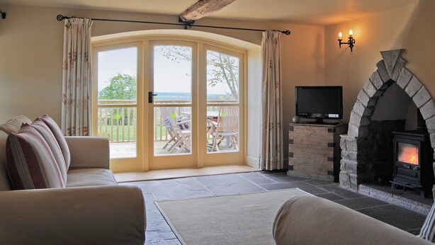 Una sala de estar acogedora con chimenea de piedra, televisión y vistas al exterior a través de un ventanal.
