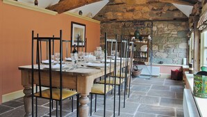 Un comedor con pared de piedra, vigas de madera y una mesa dispuesta para seis comensales.