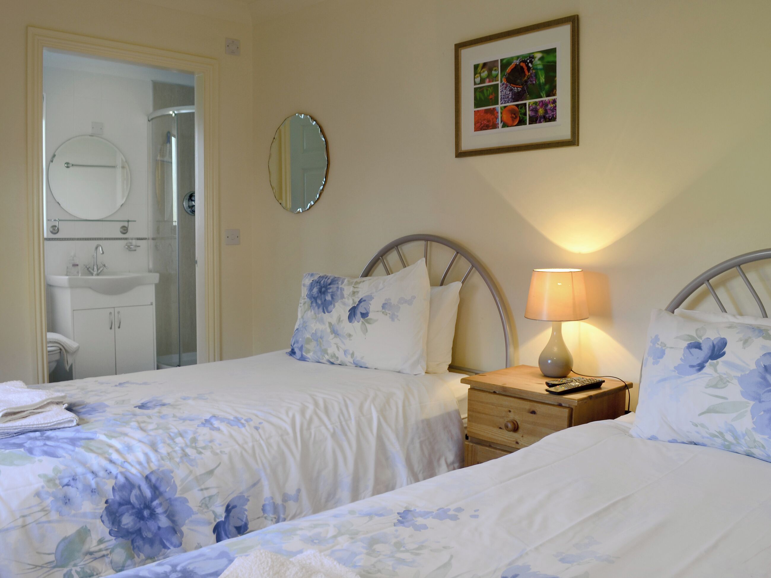 A bedroom with two beds, a bedside table with a lamp, a mirror, and a bathroom visible through an open door.