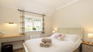 A bedroom with a bed, bedside tables, a window with curtains, a radiator, and a small stool.
