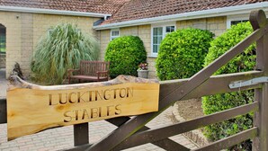 A wooden sign with the text "Luckington Stables" in front of a building with a tiled roof and brick walls.