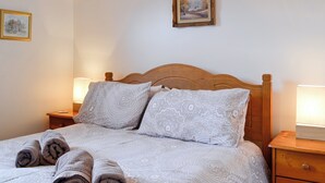 Un lit bien fait, avec une literie à motifs et des serviettes enroulées, deux lampes de chevet et deux tableaux représentant des paysages, encadrés et accrochés au mur.