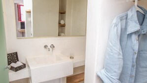 Une salle de bain avec un lavabo blanc, un miroir et une chemise suspendue.