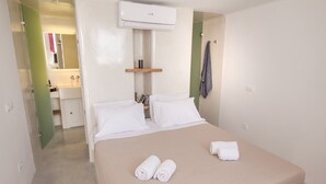 Une chambre d’hôtel avec un lit, deux serviettes roulées, une étagère avec des articles de toilette et un appareil de climatisation.