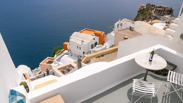 Un balcon avec vue sur la mer, des bâtiments blancs et une table avec des chaises.