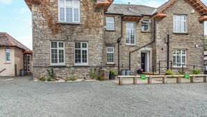 A stone building with multiple windows, a gravel driveway, and a wooden bench. - Silverdale Apartment (Meathop, near Grange-over-Sands)