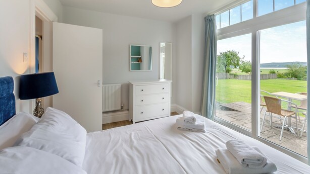 A bedroom with a bed, a dresser, a mirror, and a view of the outdoors. - Silverdale Apartment (Meathop, near Grange-over-Sands)