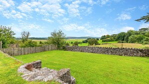 A grassy field with a stone wall and a wooden fence, surrounded by trees and hills in the distance. - Silverdale Apartment (Meathop, near Grange-over-Sands)