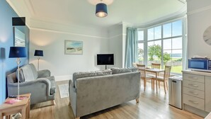 A spacious living area with a sofa, a TV, and a dining table with chairs. - Silverdale Apartment (Meathop, near Grange-over-Sands)