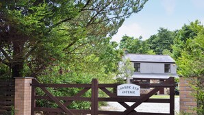 A wooden gate with a sign reading "COOMBE END COTTAGE" leading to a house with a stone facade and a grey roof. - 2 bedroom accommodation in Carn Brea, Redruth (Carn Brea, Redruth)