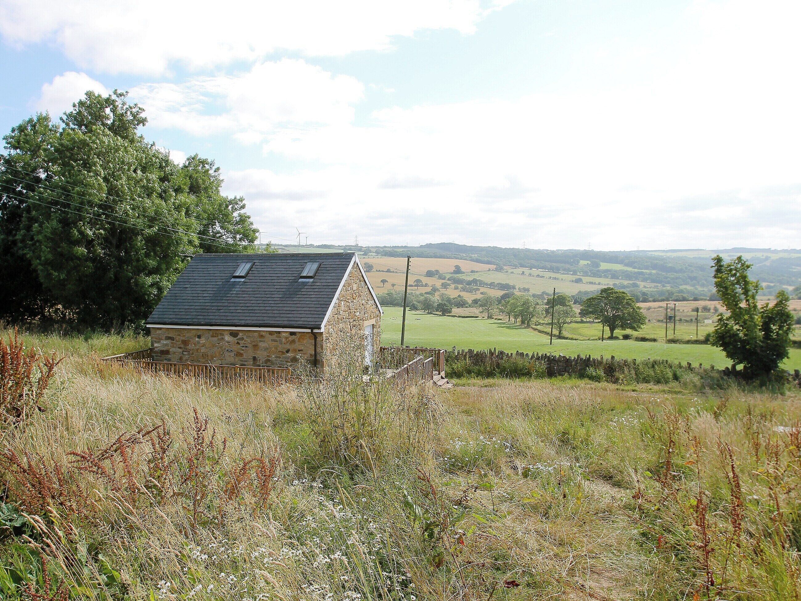 A stone building with a sloped roof and two skylights, surrounded by a grassy field and trees.
