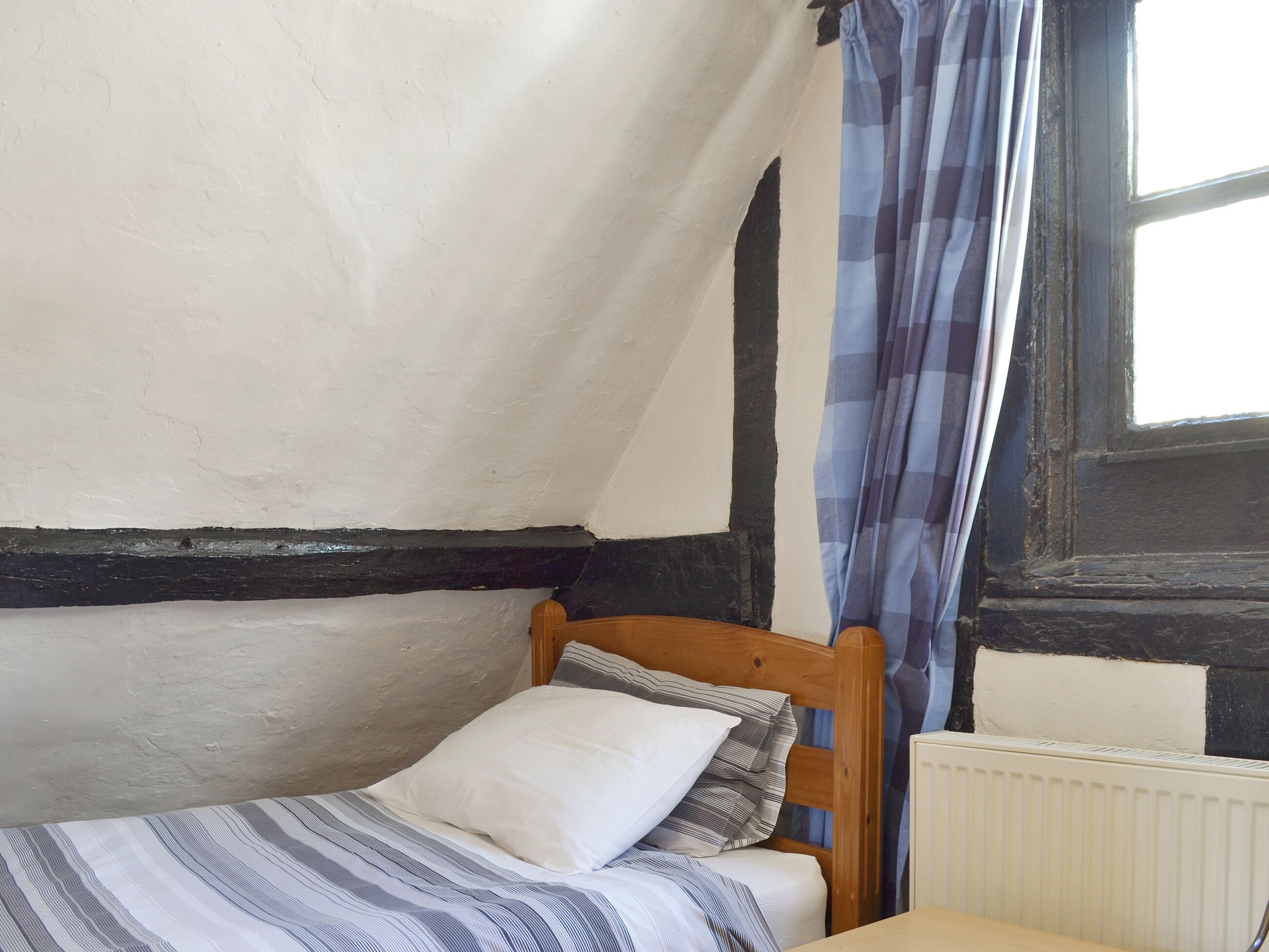 A small, single-bed room with a wooden headboard, a radiator, and a window with curtains.