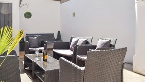 An outdoor seating area with wicker furniture, a table with a bottle, and a hanging plant. - 4 bedroom accommodation in York (York)