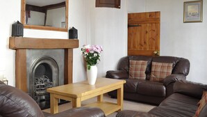 A living room with a fireplace, a wooden table, a brown leather sofa, and a mirror on the wall. - 4 bedroom accommodation in York (York)