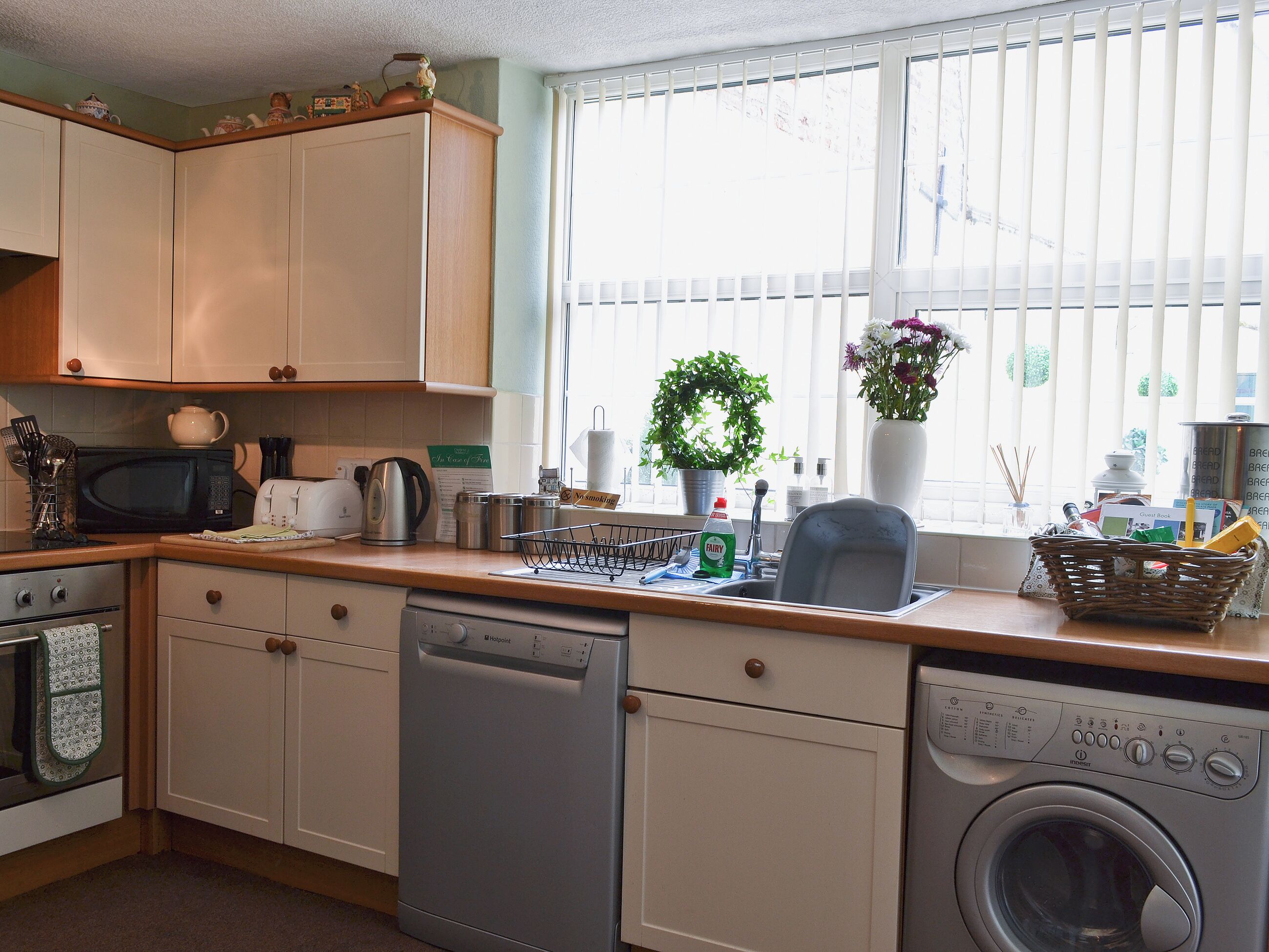 A kitchen with a dishwasher, microwave, and oven. There is a window with blinds and a potted plant on the windowsill.