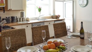 A modern kitchen with white cabinets, a dishwasher, and a dining area with wicker chairs and a table set for two. - 4 bedroom accommodation in York (York)