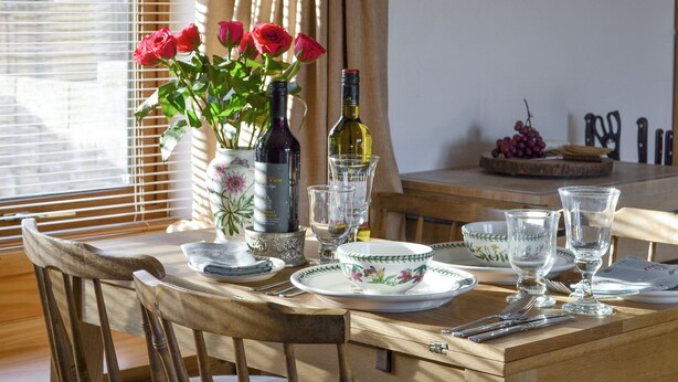 A dining table set with plates, glasses, and cutlery, a vase with red roses, and two wine bottles.
