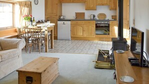 A cozy living room with a sofa, a wooden coffee table, and a dining area with a table and chairs. A kitchen with wooden cabinets and a stove is visible in the background.