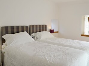 A double bed with a plaid headboard, white linens, and a bedside table with a lamp.