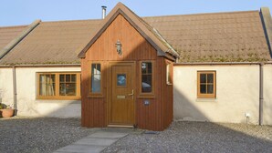 A small wooden building with a brown door, two windows, and a number '23' sign.