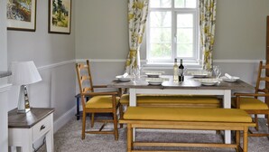 A dining room with a table set for four, two chairs on each side, a bench in the center, and a window with floral curtains.