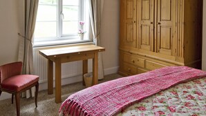 A bedroom with a wooden desk, a red chair, a large wardrobe, and a bed with a floral duvet.