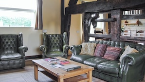 Una habitación con una mesa de centro de madera, dos sillones de cuero, un sofá verde y vigas de madera a la vista.