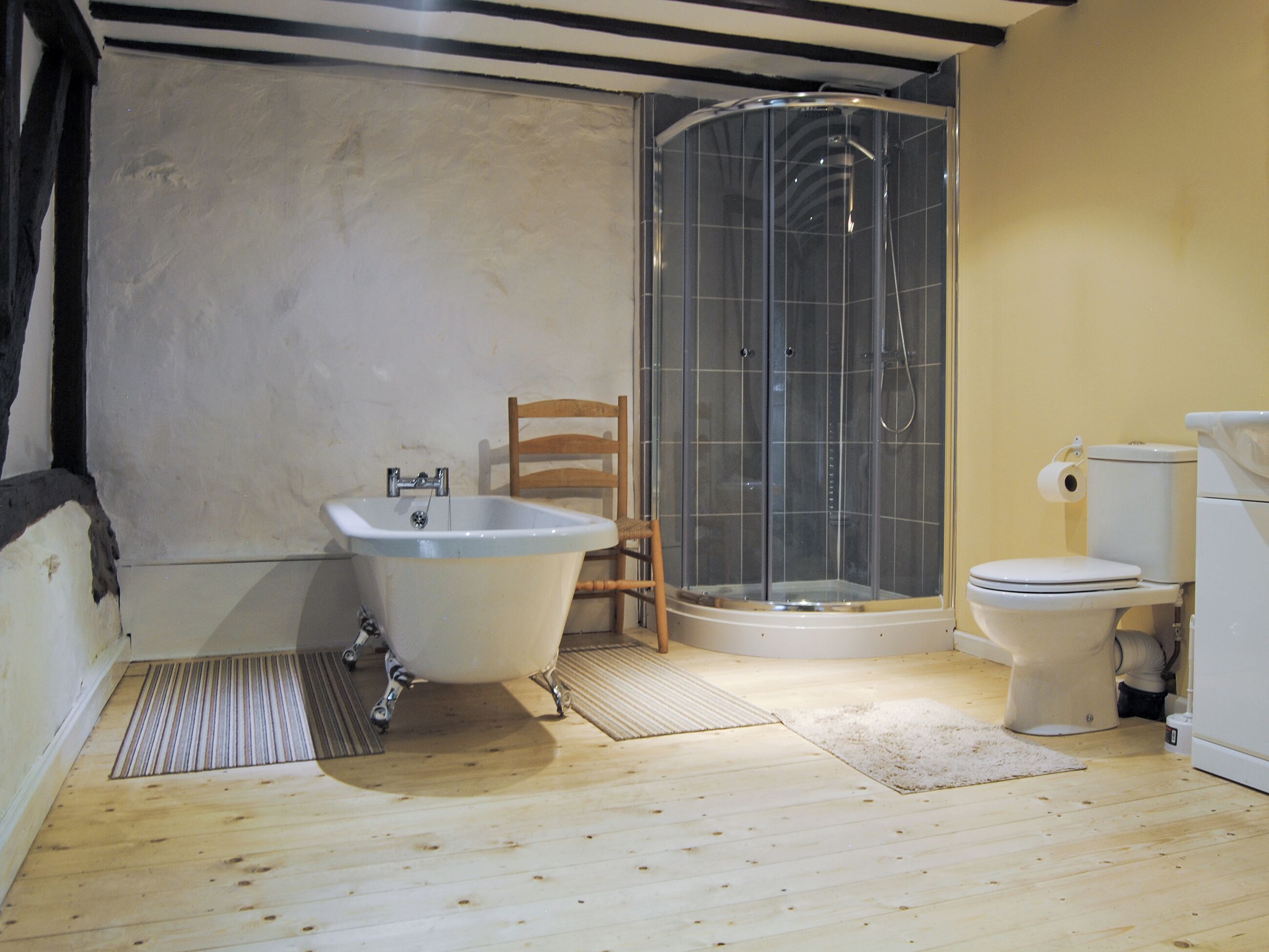 Un bagno con una vasca da bagno a piedi di leone, un box doccia, un water e una sedia in legno.
