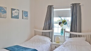 Een slaapkamer met twee bedden, een raam met gordijnen en een bloevas op de vensterbank.