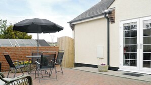 Een terras met een tafel en stoelen, een zwarte parasol en een witte deur.