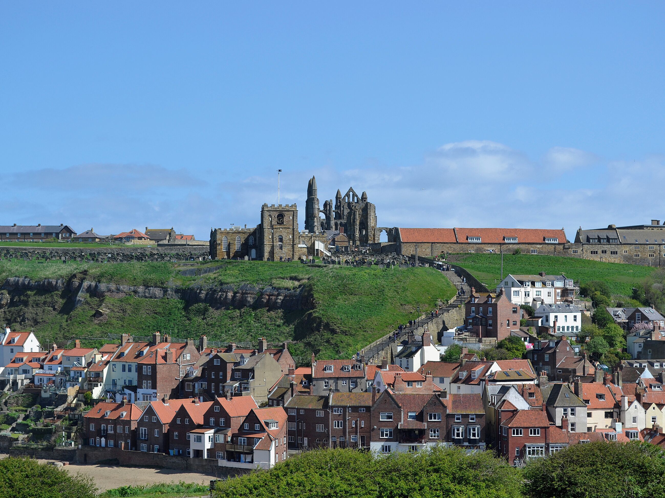 A historic town with a prominent church and castle ruins on a hill, surrounded by residential buildings.