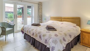 A bedroom with a bed, a chair, a nightstand, and a window with curtains. - 3 bedroom accommodation in Wicken, near Ely (Wicken, near Ely)