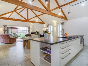 Une cuisine spacieuse dotée d’un grand îlot central, de poutres en bois et de luminaires suspendus.